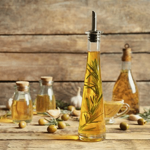 Huile d'olive vrac dans une bouteille en verre avec des olives vertes à côté.